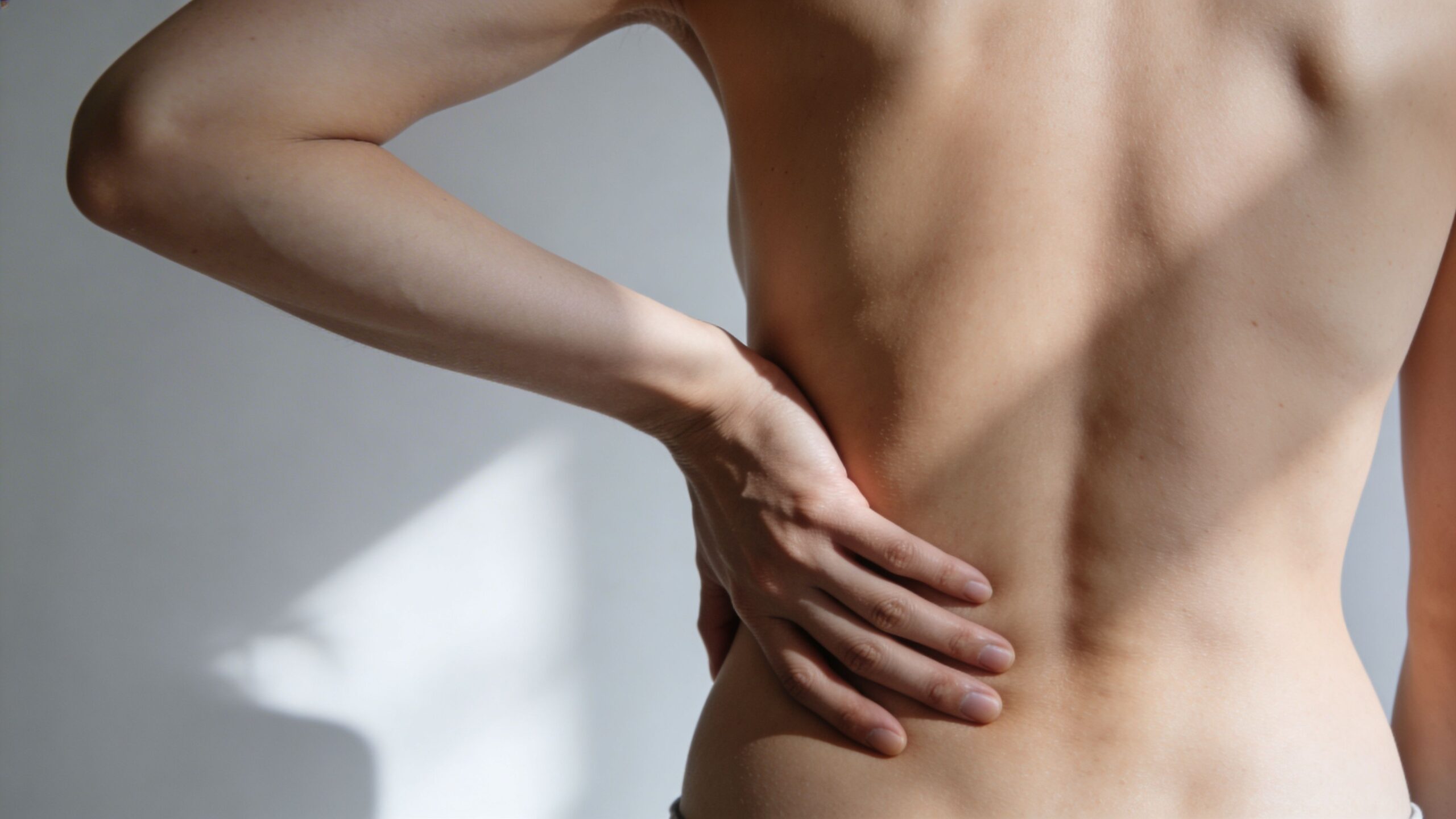 A person holding their lower back due to pain, illustrating symptoms related to spinal discomfort.