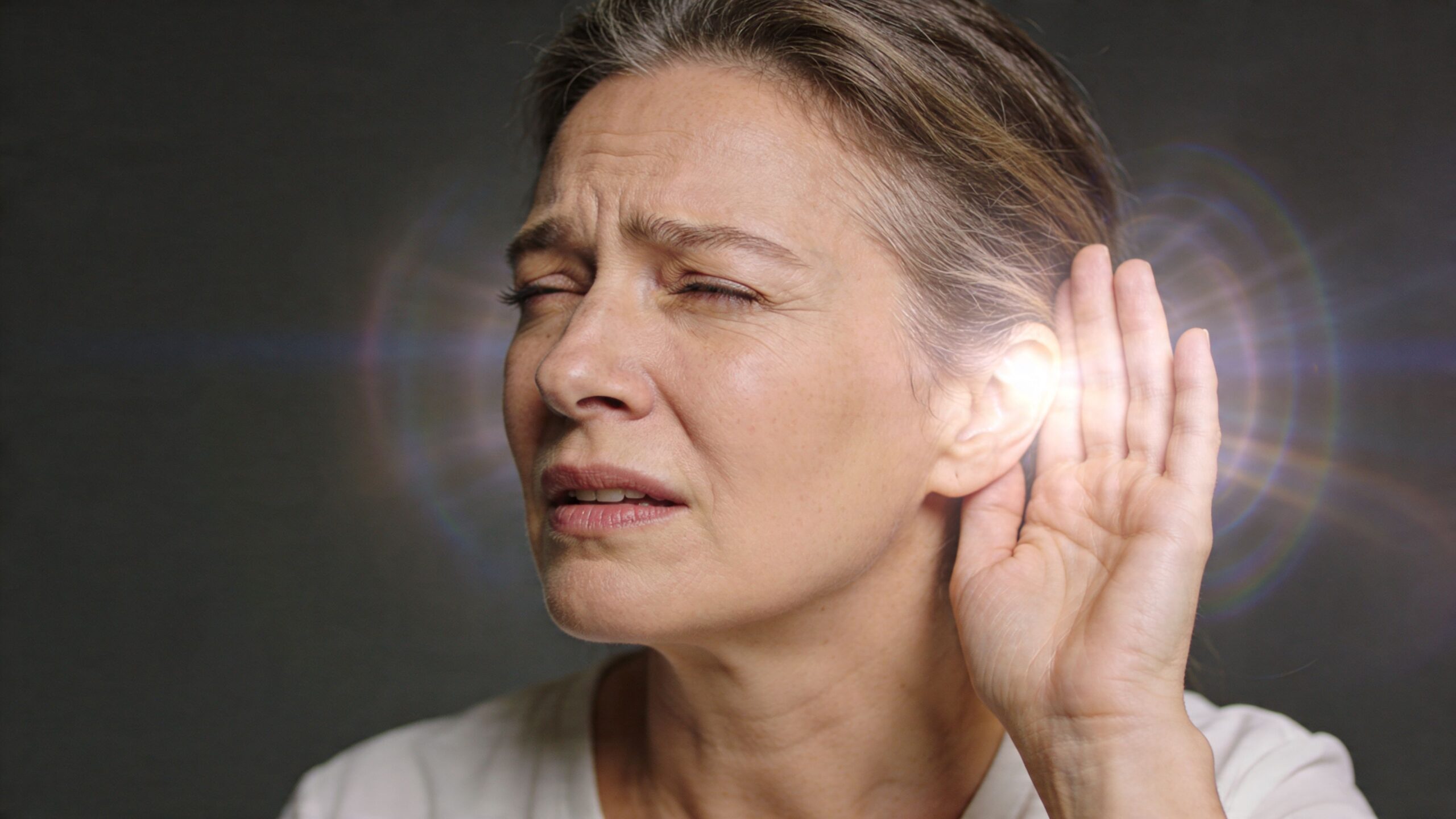 A middle aged woman with a painful expression holding her hand to her ear while sensing ringing