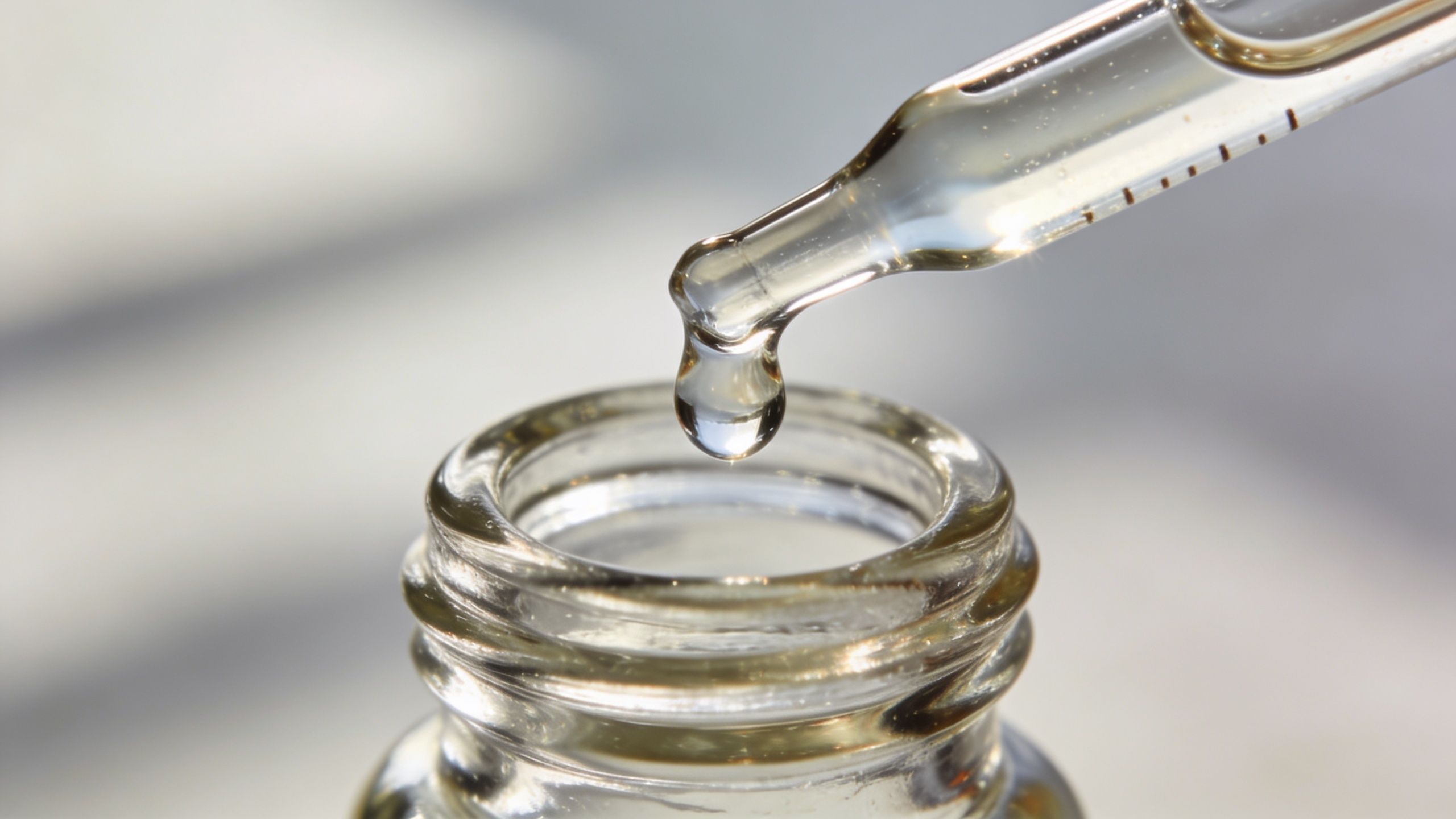 A close-up view of a clear liquid drop falling from a glass pipette into a bottle.