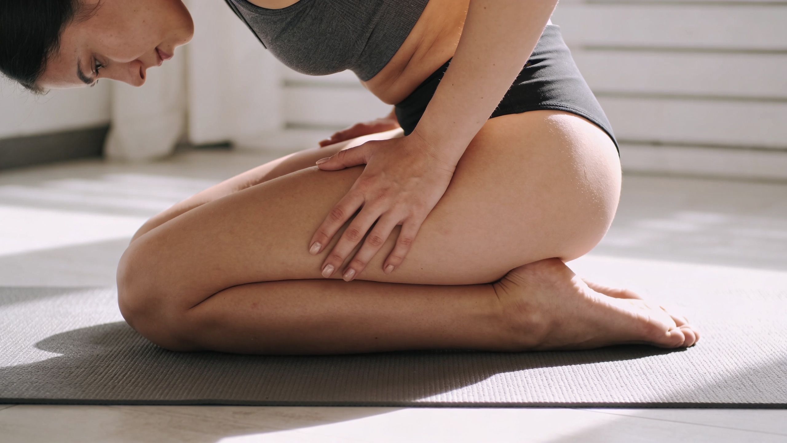 A woman kneeling on a yoga mat stretching her leg to help relieve sciatica and muscle pain.